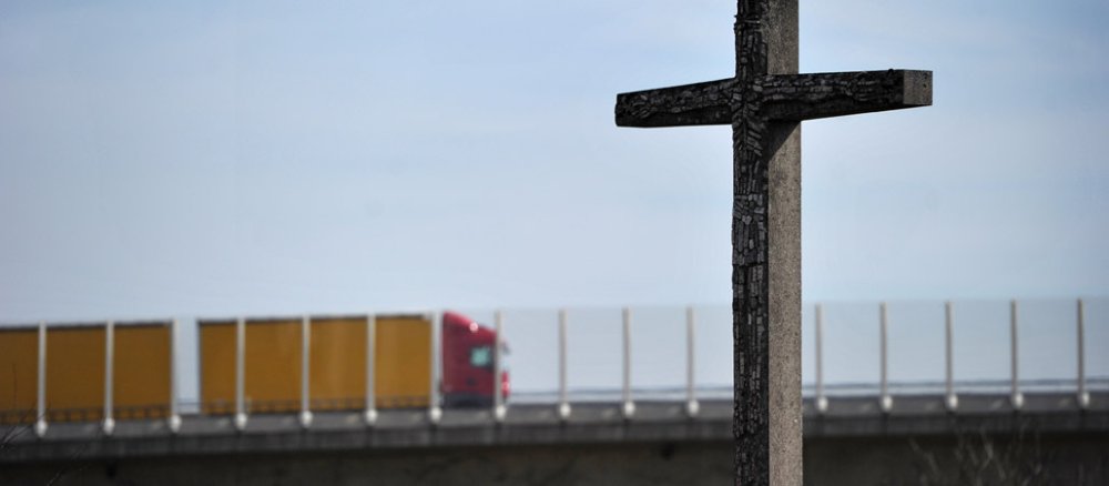 Ein LKW auf einer Autobahn und ein Kreuz - Autobahnkirchen erfreuen sich in Deutschland großer Beliebtheit.