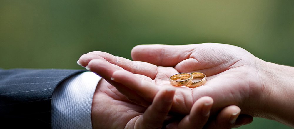 Braut und Bräutigam reichen einander die Hände und halten die Ringe.