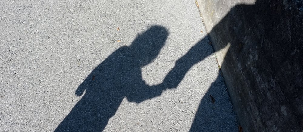 Der Schatten eines Erwachsenen, der ein Kind an der Hand hält.