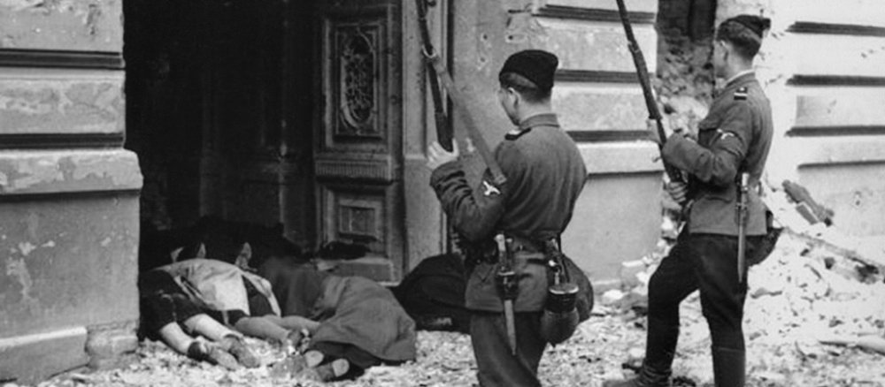 Zwei Soldaten stehen mit erhobenem Gewehr vor einem Hauseingang in dem vier Leichen liegen.