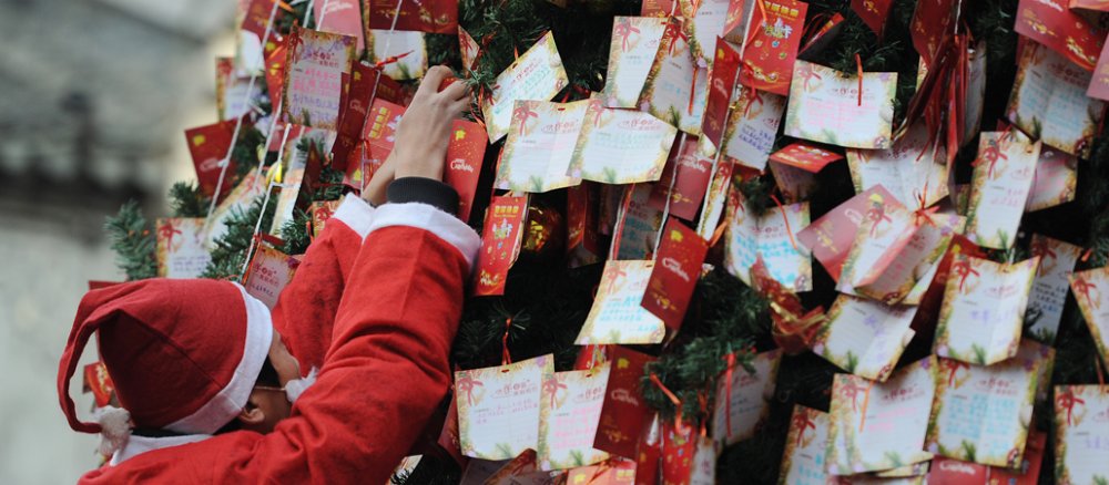 Ein Mann in Weihnachtsmannverkleidung befestigt Wunschzettel an einem Weihnachtsbaum.