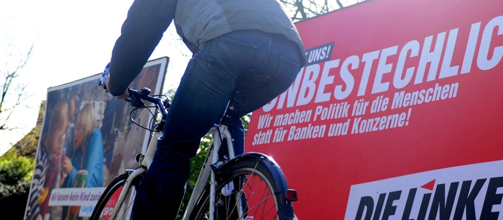 Ein Fahrradfahrer fährt an einem roten Wahlplakat der Partei "Die Linke" vorbei.
