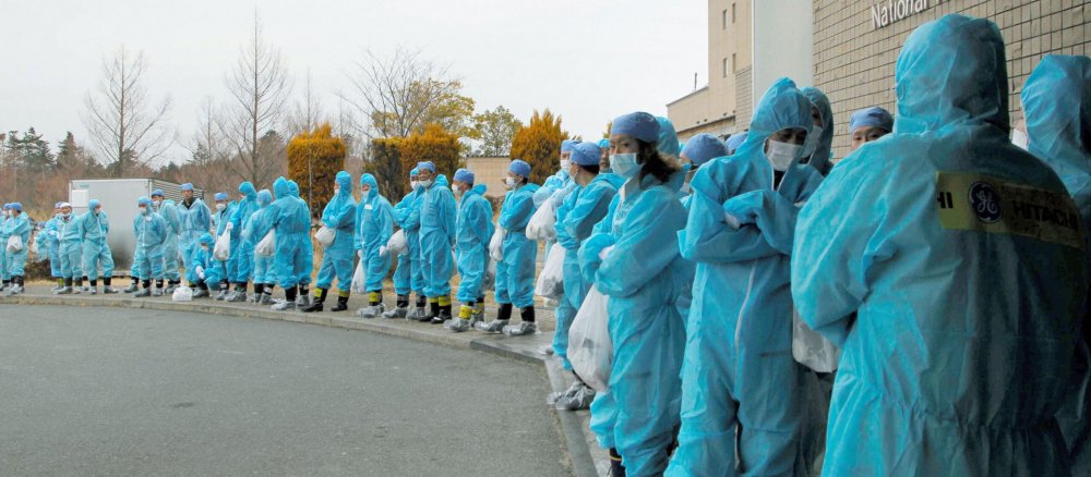 Menschen in blauen Strahlenschutzanzügen stehen in einer Reihe am Straßenrand.
