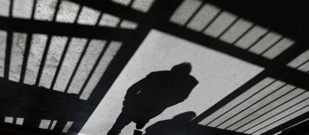 Der Schatten eines Mannes ist umrahmt vom Schatten der Gitterstäbe einer Gefängnistür.
