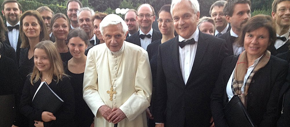 Benedikt XVI. steht neben Chorleiter Rainer Schütz. Beide sind eingeramht von den Sängerinnen und Sänger der "capella vocale" aus Priem bei Regensburg.