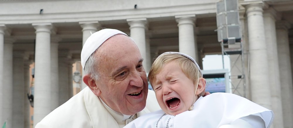 Franziskus segnet ein Kind, das als Papst verkleidet ist und weint.