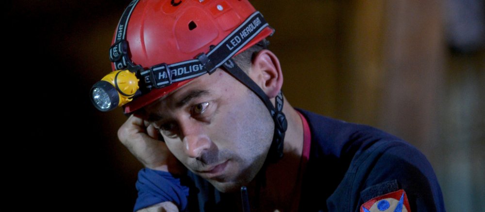 Ein Mann mit Helm und Bergwerksausrüstung schaut traurig ins Leere.