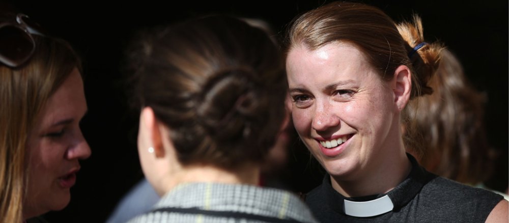 Eine Frau mit grauem ärmellosen Shirt und Priesterkragen während einer Unterhaltung.