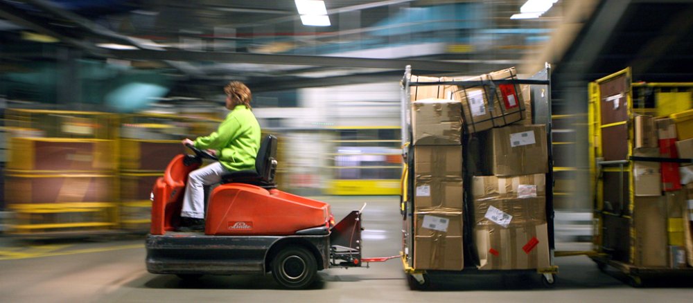 Im DHL-Paketzentrum fährt eine Mitarbeiterin einen Paketwagen durch die Halle.