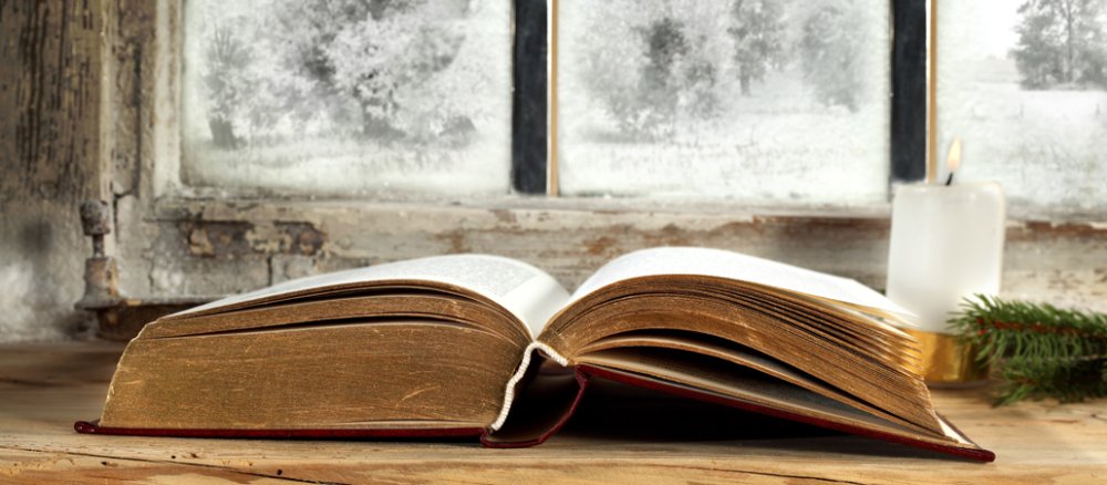 EIn altes Buch liegt auf einer Fensterbank. Daneben Kerze und Tannenzweig