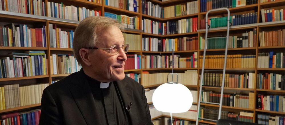 Kardinal Kasper sitzt vor seiner Bücherwand