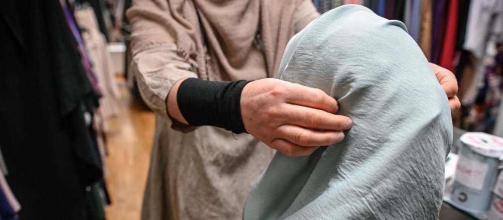 Eine Verkäuferin hilft einer Kundin, ein Kopftuch anzuprobieren