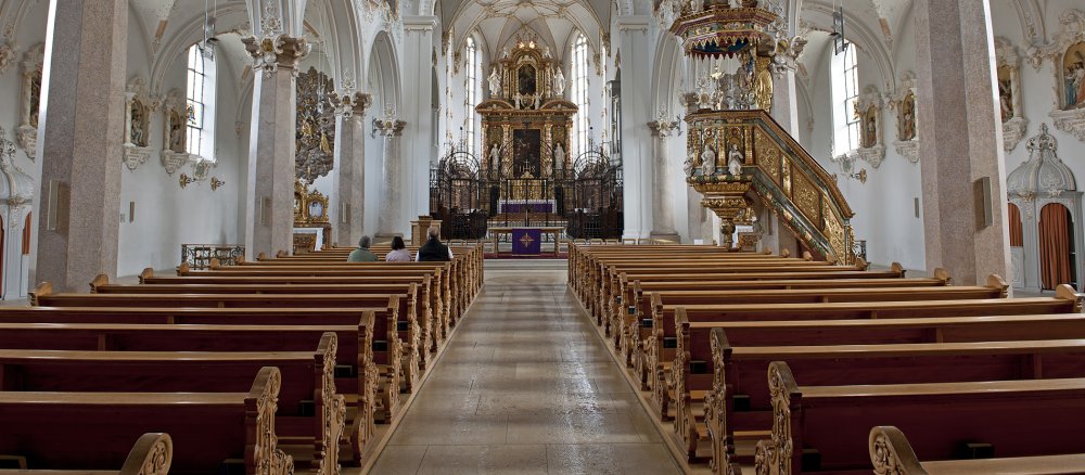 Blick in das fast vollständig leere Schiff der Klosterkirche in Mariastein, Schweiz. Nur drei Menschen sitzen in den Bänken.