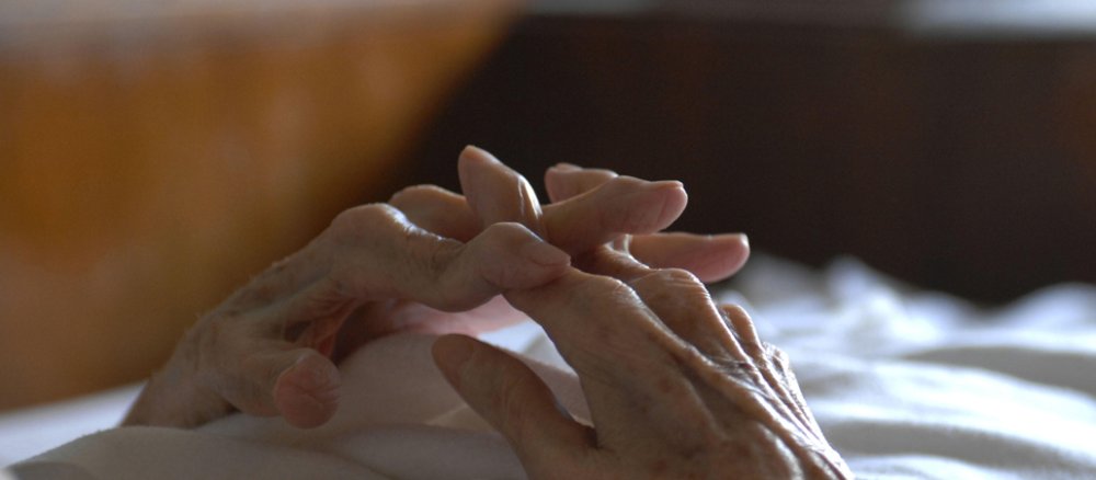 Gefaltete Hände einer Seniorin, die im Bett liegt.
