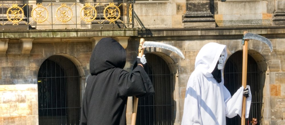 Zwei verkleidete Sensenmänner vor einer historischen Fassade.