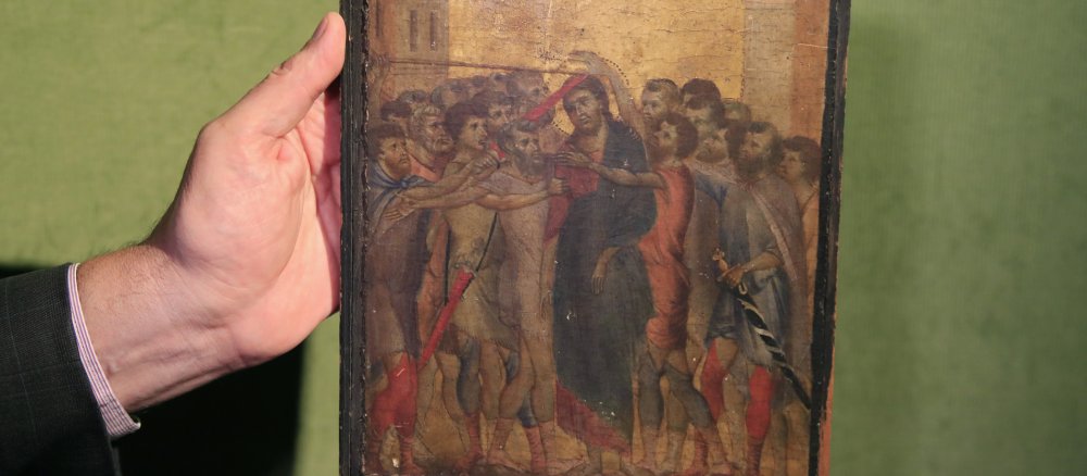 Ein Mann hält das Bild "Die Verspottung Christi" von Cimabue