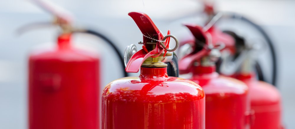 Mehrere rote Feuerlöscher stehen in einer Reihe.