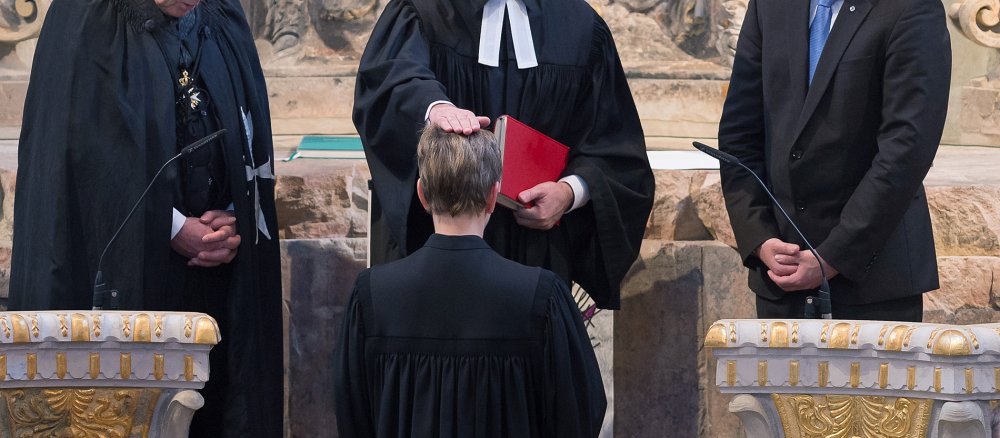 Einer evangelischen Pfarrerin wird bei ihrer Amtseinführung die Hand aufgelegt.