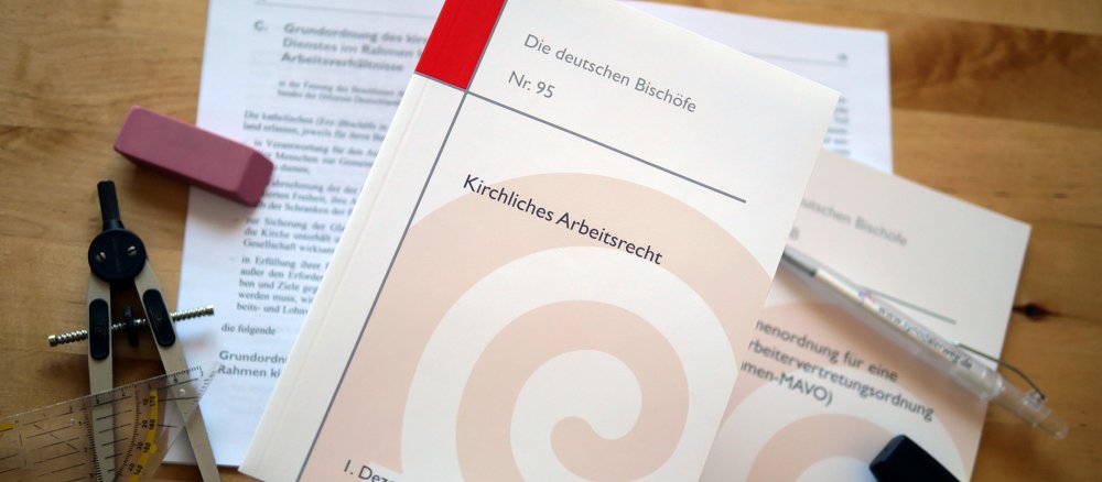 Rechtstexte des kirchlichen Arbeitsrechts liegen mit Schreibzeug auf einem Tisch