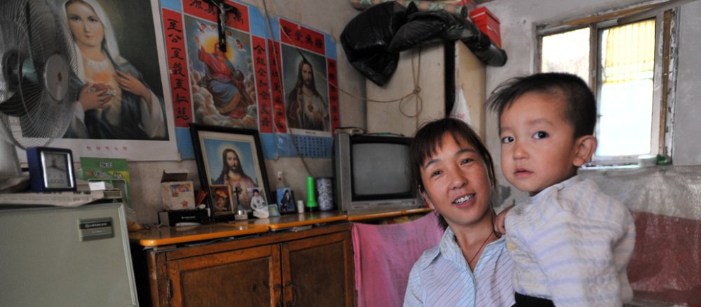 Christentum in China: Eine katholische Wanderarbeiterin mit ihrem Kind in Peking. Christliche Bilder zieren ihre kleine Wohnung.