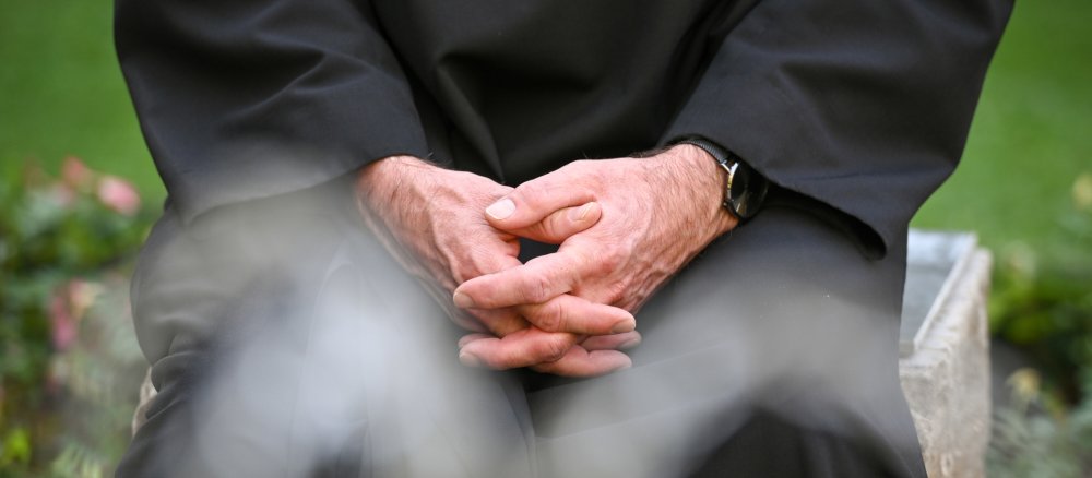 A friar sits in the garden of the cloister at Münsterschwarzach Abbey in Schwarzach, Germany, with his hands folded in prayer.