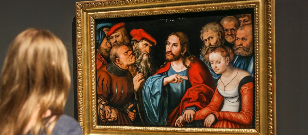Eine Frau betrachtet das Gemälde Christus und die Ehebrecherin von Lucas Cranach dem Älteren