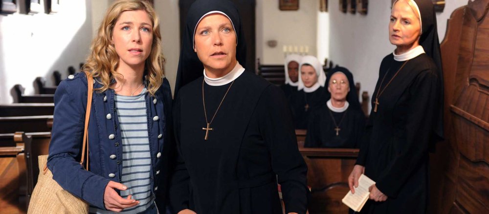 Eine junge Frau und eine Nonne in einer Kirche mit erschrecktem Gesichtsausdruck.