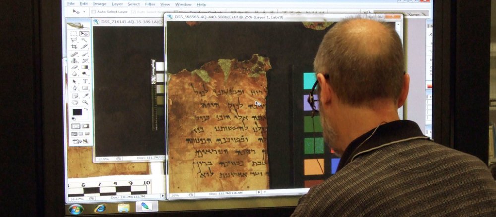 Ein Mann betrachtet auf dem Bildschirm die digitalisierte Form einer Schriftrolle aus den Höhlen von Qumran.