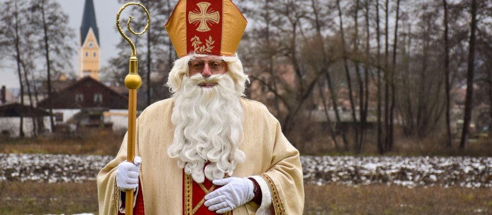 Ein Mann steht als Nikolaus verkleidet auf einer Straße, im Hintergrund eine Kirche