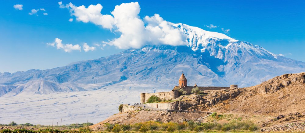 Eine armenische Klosteranlage im Vordergrund und der schneebedeckte Berg Ararat im Hintergrund.