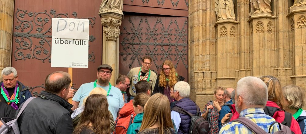 Andreas Holzbeck steht mit einem Schild "Dom überfüllt" beim Katholikentag in Erfurt