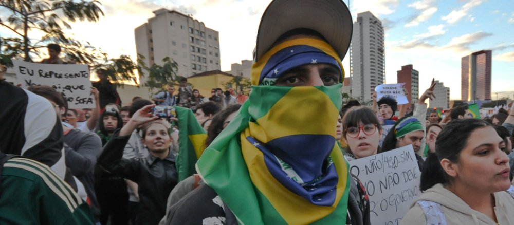Ein junger Demonstrant ist mit einer brasilianischen Flagge vermummt.