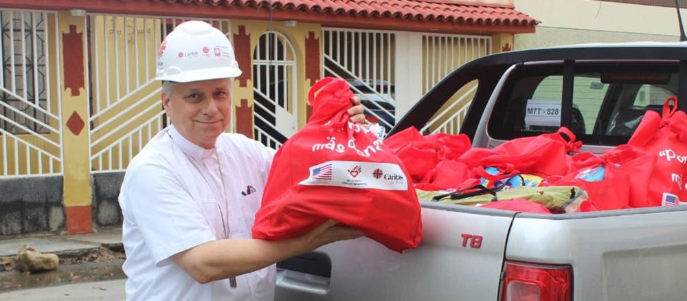Robert Prevost mit Helm und Hilfsgütern vor einem Caritas-Pickup