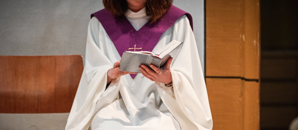 A funeral director in white liturgical vestments with a purple collar