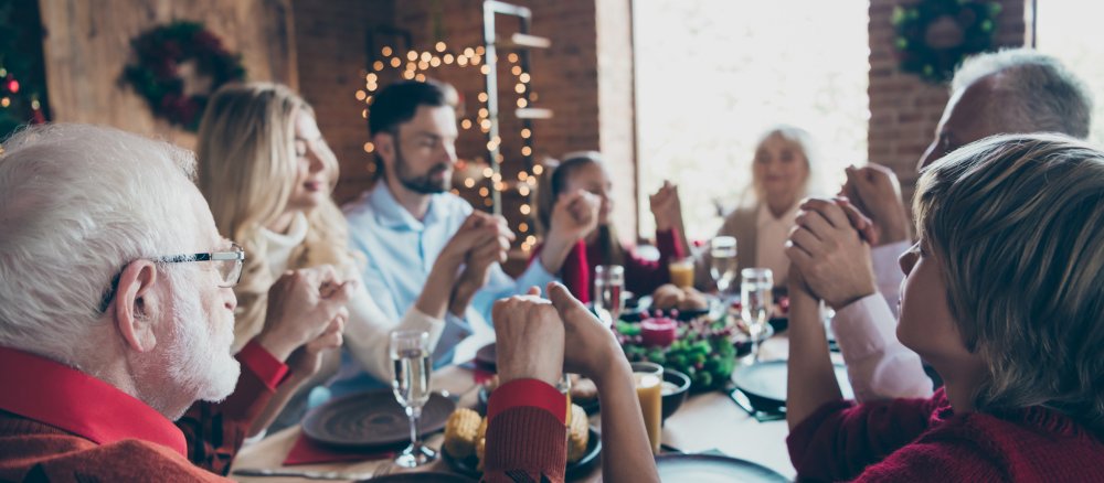Eine Familie sitzt an Weihnachten gemeinsam am Tisch und betet