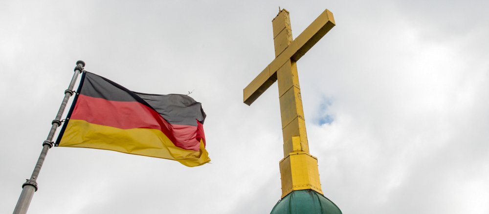 Eine wehende Deutschlandflagge neben einem Kreuz