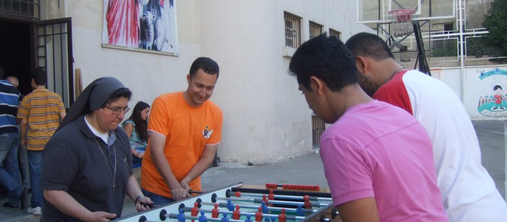 Eine Ordensschwester im dunkelgrauen Habit spielt mit drei jungen Syrern Tischfußball.