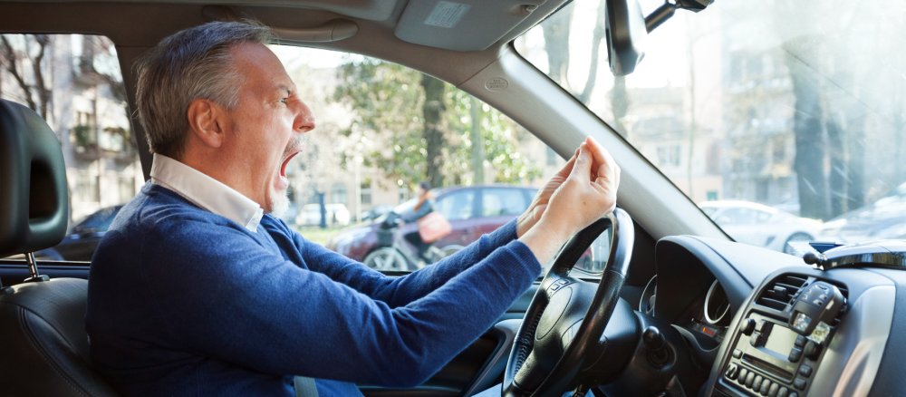 Ein Mann sitzt am Lenkrad eines Autos und schimpft.