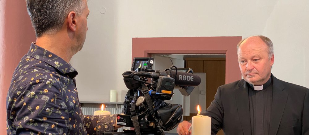 Pfarrer Förg zündet eine Kerze an und wird dabei gefilmt
