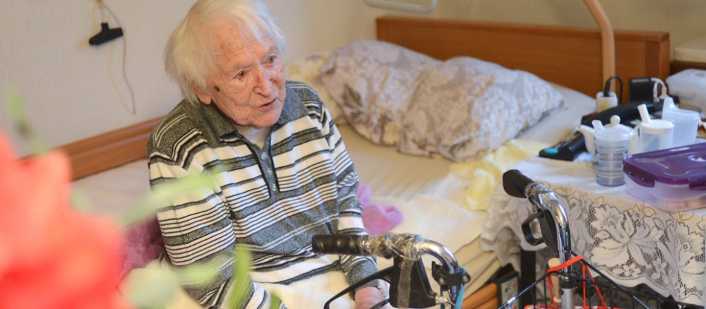Eine alte Frau sitzt auf ihrem Bett.
