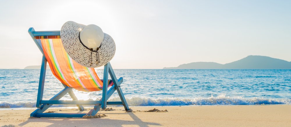 Ein Liegestuhl steht an einem sonnigen Strand.
