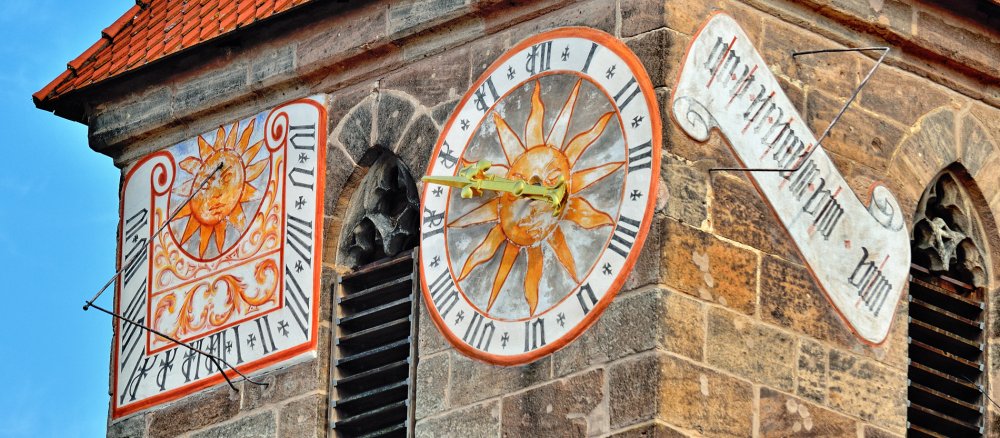 Historische Uhr und Sonnenuhr an einem Kirchturm