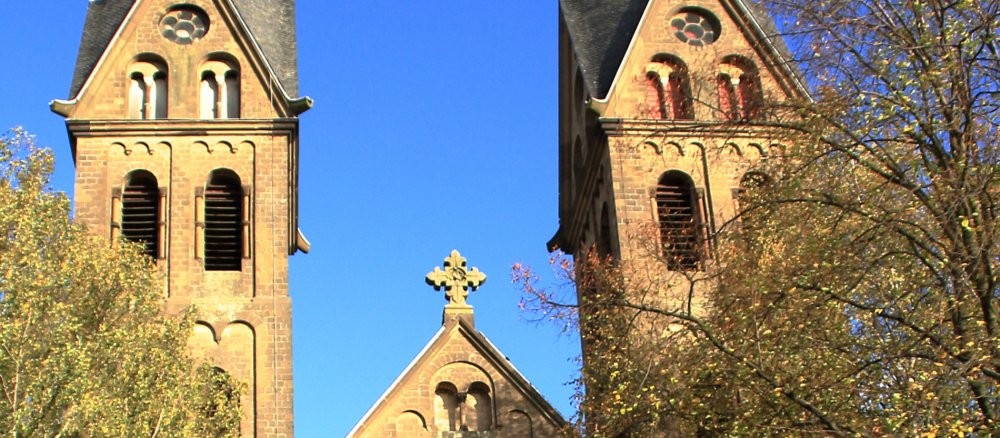 Kirchtürme im Abendlicht, herbstliche Blätter im Vordergrund, stimmungsvolles Bild