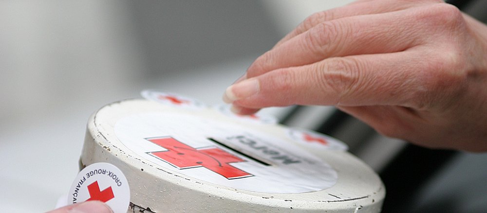 Jemand steckt Geld in eine Spendenbox des Roten Kreuzes.