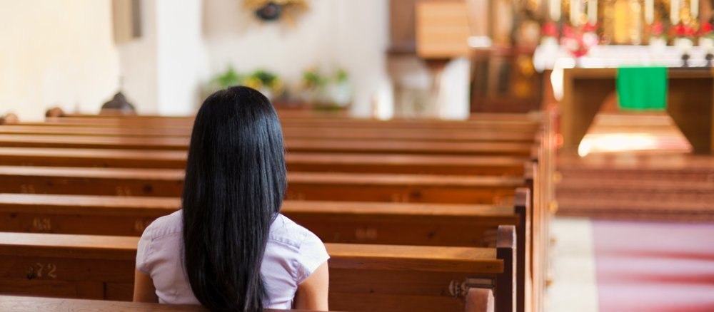 Eine Frau mit dunklen Haaren sitzt einsam und allein in einer Kirche