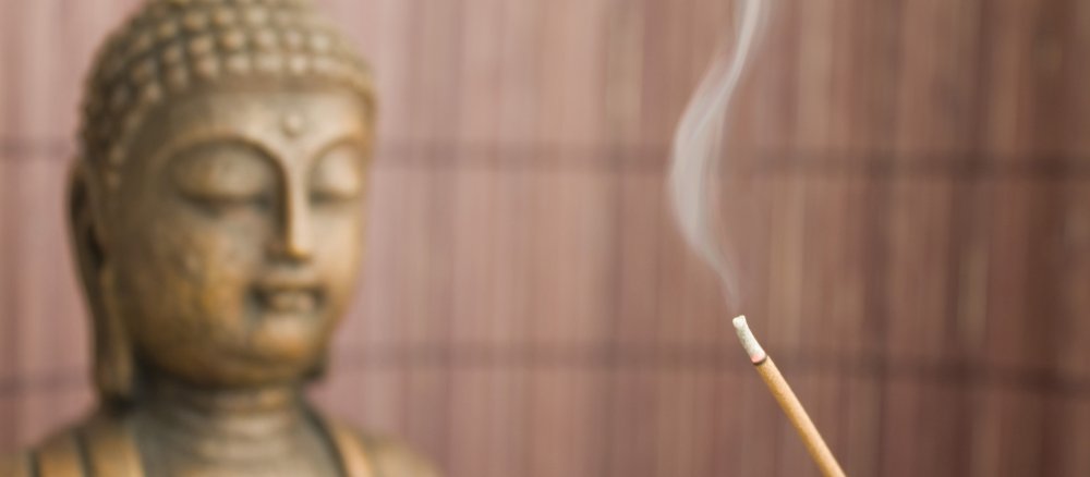 Ein brennendes Räucherstäbchen vor dem Kopf einer Buddha-Statue.