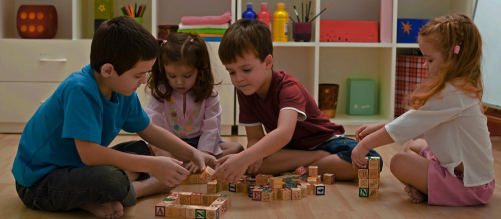 Kinder sitzen auf dem Boden und spielen mit Buchstabenklötzchen