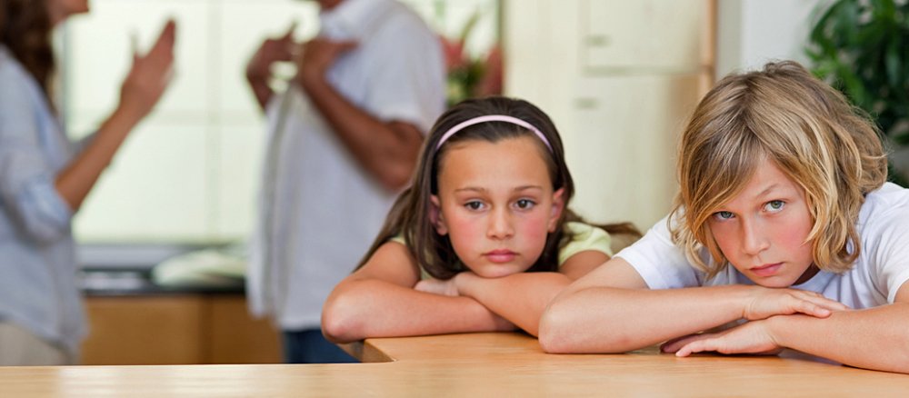 In der Küche streiten sich im Hindergrund Mutter und Vater, während die Kinder im Vordergrund verzweifelt darüber dreinschauen.