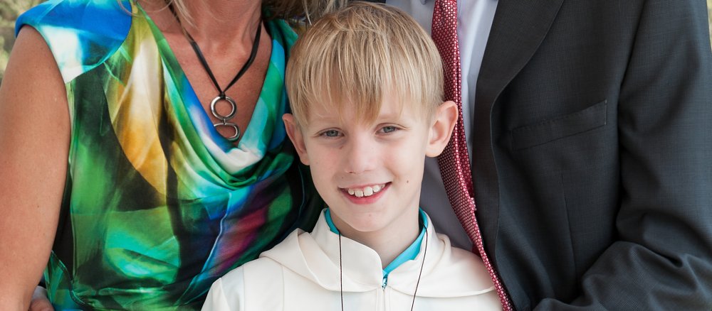 Eltern posieren mit ihrem 9-jährigen Sohn für ein Foto. Der blonde Junge trägt sein Erstkommuniongewand.