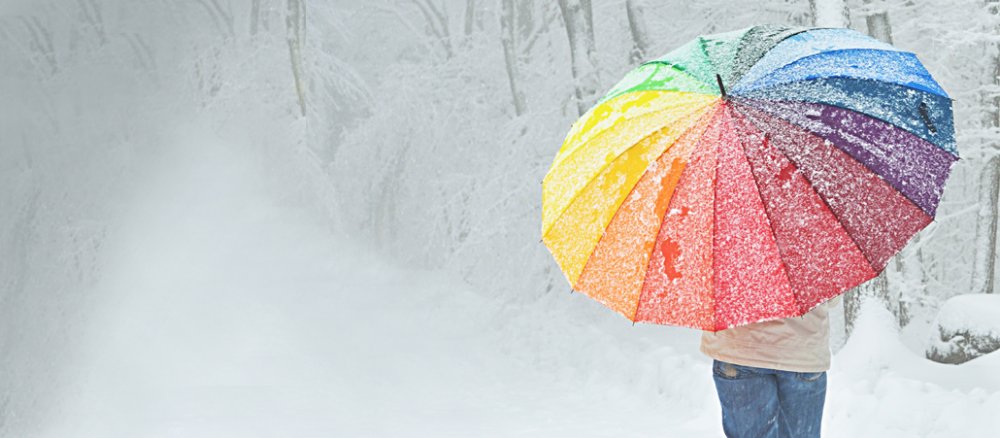 Mann mit großem Regenbogenschirm geht durch einen verschneiten Wald.